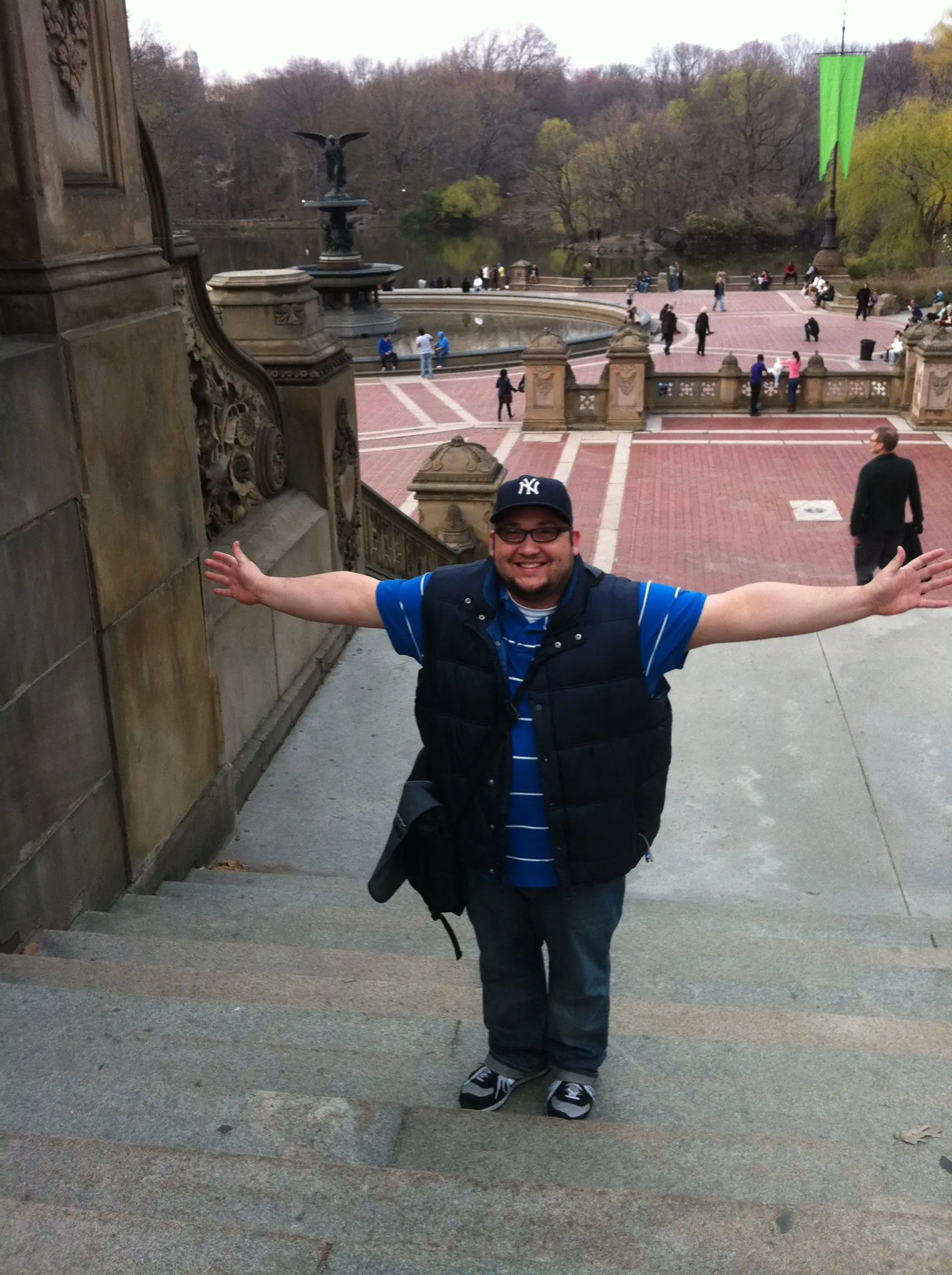 Daniel standing on the steps at Bethesda Terrace in Central Park with his arms out, in a Yankees cap.