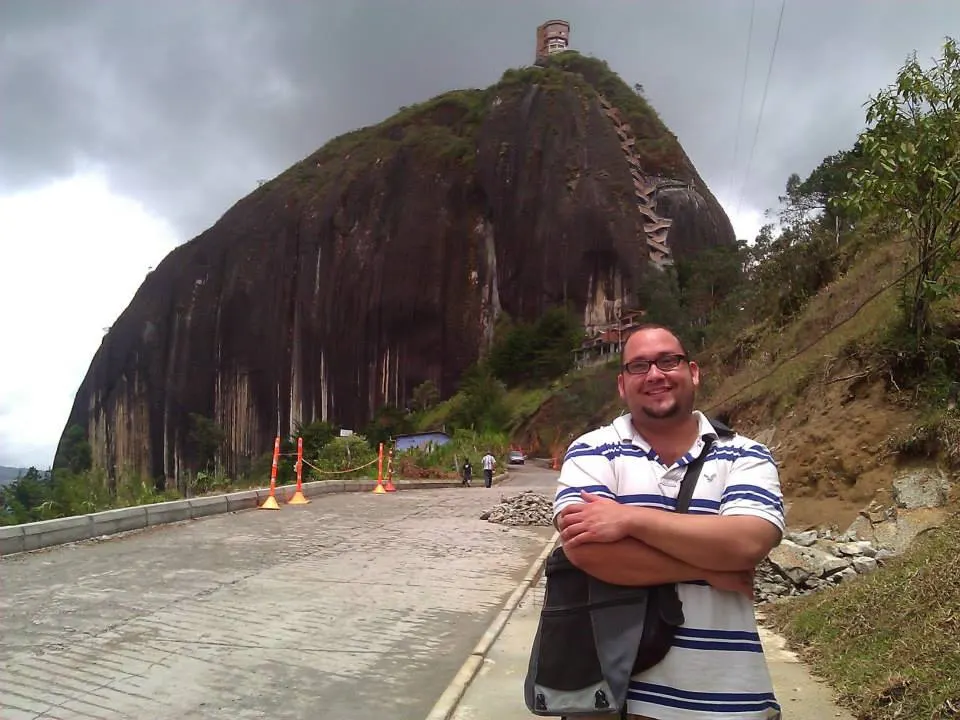 Daniel standing on a road in front of a large granite rock formation, with clouds overhead.
